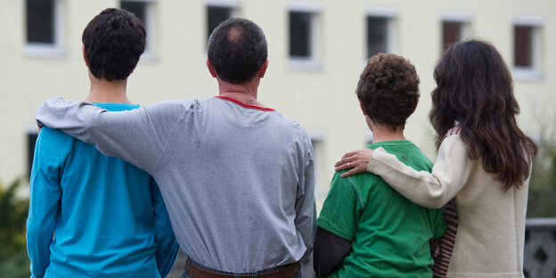 Ein Mann und eine Frau sind von hinten zu sehen, sie haben jeder den Arm um einen ihrer Söhne gelegt Ein Mann und eine Frau sind von hinten zu sehen, sie haben jeder den Arm um einen ihrer Söhne gelegt