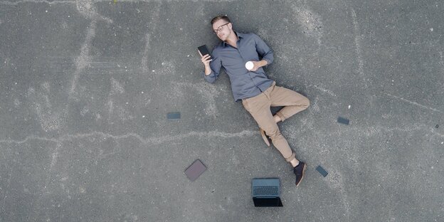 Jemand liegt auf dem Boden und schaut auf ein Smartphone um ihn herum liegen weitere Smartphones und ein Laptop Jemand liegt auf dem Boden und schaut auf ein Smartphone um ihn herum liegen weitere Smartphones und ein Laptop