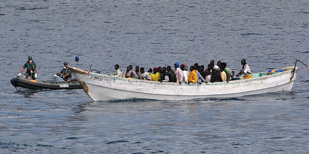 Eine Gruppe von Flüchtlingen sitzt in einem weißen Boot, dem sich ein Rettungsboot nähert