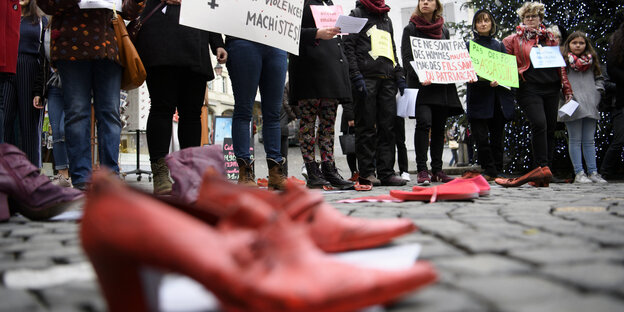 Frauen und Mädchen halten Schilder hoch, im Vordergrund ein rotes Paar Schuhe Frauen und Mädchen halten Schilder hoch, im Vordergrund ein rotes Paar Schuhe