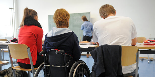 Drei Schüler sitzen in einem Klassenzimmer und schauen zur Tafel. Einer davon sitzt im Rollstuhl. Drei Schüler sitzen in einem Klassenzimmer und schauen zur Tafel. Einer davon sitzt im Rollstuhl.