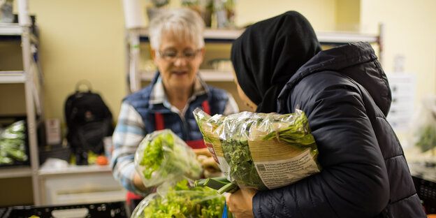 Eine Frau steht hinter Gemüsekörben, eine andere hält einen Beutel Salat im Arm Eine Frau steht hinter Gemüsekörben, eine andere hält einen Beutel Salat im Arm