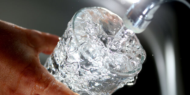 Wasser fließt sprudelnd aus einem Hahn in ein Glas