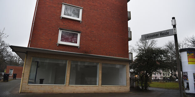 Ein schmales Haus aus roten Backsteinen. Im Erdgeschoss sind die großen Fenster eines Ladenlokals.