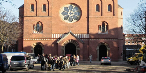Menschen stehen auf einem Platz vor einer Kirche aus roten Backsteinen. Menschen stehen auf einem Platz vor einer Kirche aus roten Backsteinen.
