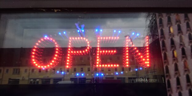 Hinter einer Fensterscheibe leuchtet in rot das Wort "Open". Hinter einer Fensterscheibe leuchtet in rot das Wort "Open".