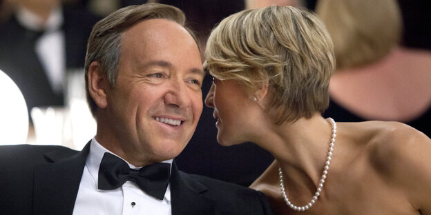 Francis Underwood (Kevin Spacy) und Claire Underwood (Robin Wright) sitzen gemeinsam an einem Tisch. Sie flüstert ihm etwas ins Ohr, Francis Underwood (Kevin Spacy) und Claire Underwood (Robin Wright) sitzen gemeinsam an einem Tisch. Sie flüstert ihm etwas ins Ohr,