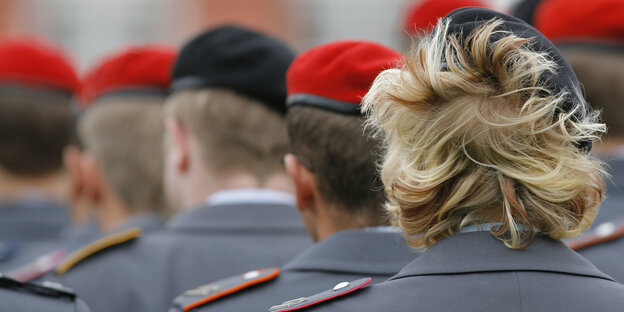 Mehrere Soldaten stehen in mehreren Reihen und tragen rote Mützen, eine Soldatin hat verwuschelte Haare Mehrere Soldaten stehen in mehreren Reihen und tragen rote Mützen, eine Soldatin hat verwuschelte Haare