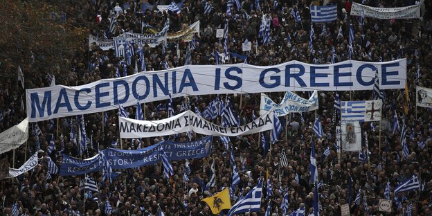 Viele Menschen halten Banner und blau-weiße Fahnen in die Höhe. in der Mitte des Bildes ist ein übergroßes Banner mit der Aufschrift "Macedonia is Greece" zu sehen Viele Menschen halten Banner und blau-weiße Fahnen in die Höhe. in der Mitte des Bildes ist ein übergroßes Banner mit der Aufschrift "Macedonia is Greece" zu sehen