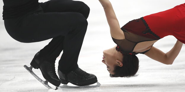 eine Eiskunstläuferin, die an einem Arm gehalten wird, fliegt kopfüber über das Es eine Eiskunstläuferin, die an einem Arm gehalten wird, fliegt kopfüber über das Es