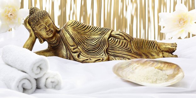eine liegende Buddhafigur, daneben Handtücher und eine Schale eine liegende Buddhafigur, daneben Handtücher und eine Schale
