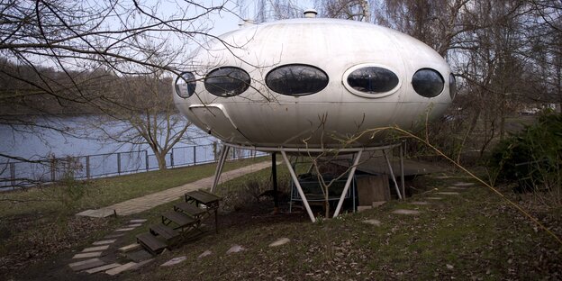 Ein ufoartiges Gefährt steht an einem Fluss auf Gras Ein ufoartiges Gefährt steht an einem Fluss auf Gras