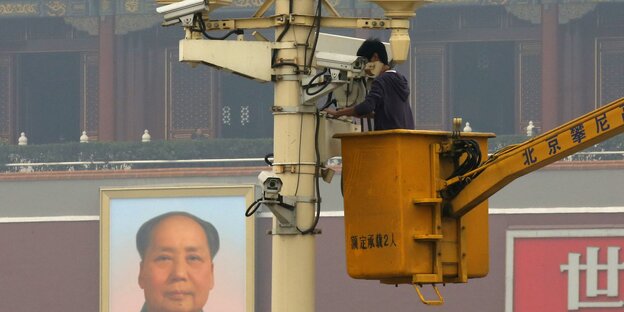 Ein Mann arbeitet aus einer Hebebühne heraus an einem Mast mit Überwachungskameras Ein Mann arbeitet aus einer Hebebühne heraus an einem Mast mit Überwachungskameras