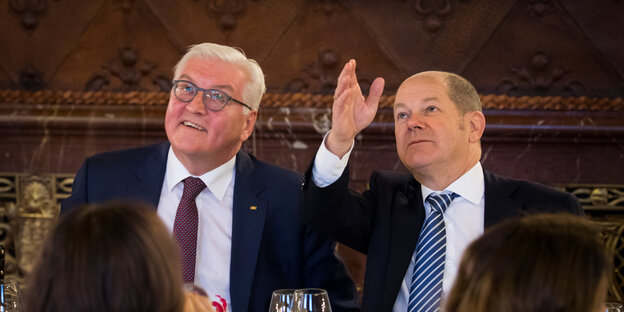 Frank-Walter Steinmeier und Olaf Scholz sitzen nebeneinander. Scholz zeigt nach oben