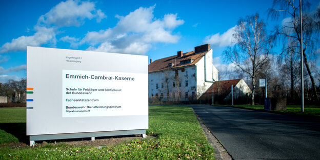 Das Schild der Emmich-Cambrai-Kaserne steht vor einem weißen Gebäude mit rotem Ziegeldach.