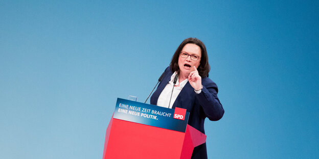 Eine Frau steht an einem Pult und gestikuliert Eine Frau steht an einem Pult und gestikuliert
