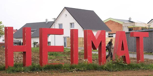 Riesige rote Buchstaben stehen auf einer Wiese vor einer Eigenheimsiedlung Riesige rote Buchstaben stehen auf einer Wiese vor einer Eigenheimsiedlung