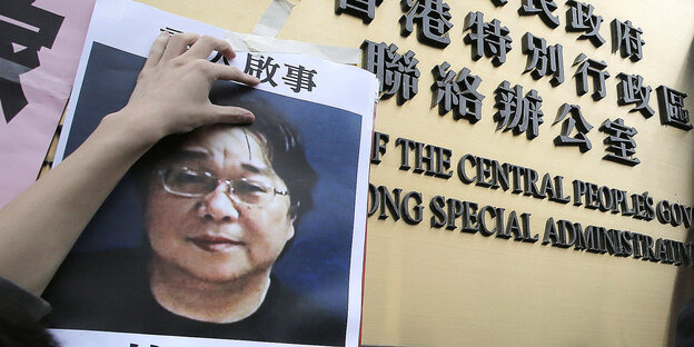 Hände halten ein Plakat mit dem Konterfei eines Mannes feist - an einem Eingangsschild des Regierungssitzes in Hongkong Hände halten ein Plakat mit dem Konterfei eines Mannes feist - an einem Eingangsschild des Regierungssitzes in Hongkong