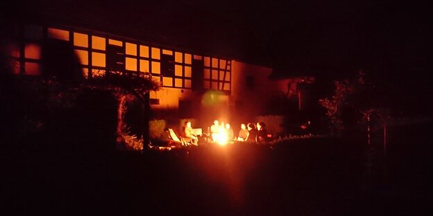 Menschen sitzen um ein Lagerfeuer vor einem Fachwerkhaus Menschen sitzen um ein Lagerfeuer vor einem Fachwerkhaus