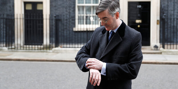 Brexit-Hardliner Jacob Rees-Mogg wartet vor der Residenz der Premierministerin und schaut auf die Uhr. Brexit-Hardliner Jacob Rees-Mogg wartet vor der Residenz der Premierministerin und schaut auf die Uhr.