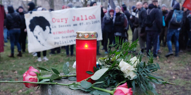 Menschen halten ein Transparent, im Vordergrund brennt eine Kerze vor einer Rose