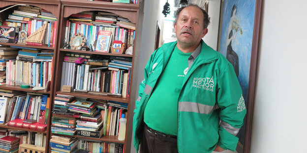 Ein Mann in grünem T-Shirt und gelichfarbiger Jacke steht vor einer prallgefüllten Bücherwand Ein Mann in grünem T-Shirt und gelichfarbiger Jacke steht vor einer prallgefüllten Bücherwand