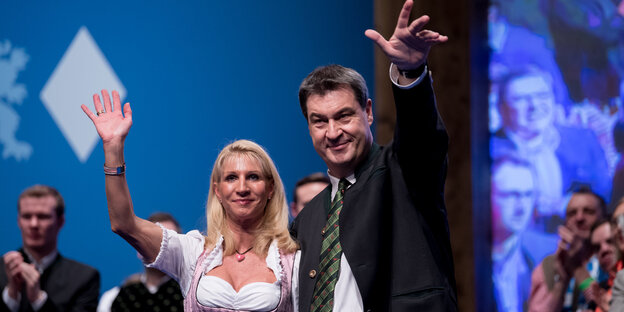 Markus Söder und seine Frau Karin Baumüller-Söder winken von einer Bühne herab Markus Söder und seine Frau Karin Baumüller-Söder winken von einer Bühne herab