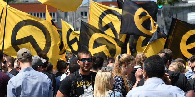 Man sieht mehrere Männer und Frauen unter gelb-schwarzen Flaggen der identitären Bewegung Man sieht mehrere Männer und Frauen unter gelb-schwarzen Flaggen der identitären Bewegung