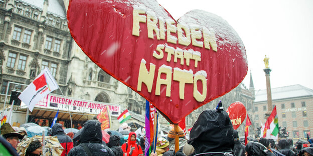 Kundgebung im Schnee, im Vordergrund ein herzförmiges Transparent mit der Aufschrift „Frieden statt Nato“ Kundgebung im Schnee, im Vordergrund ein herzförmiges Transparent mit der Aufschrift „Frieden statt Nato“