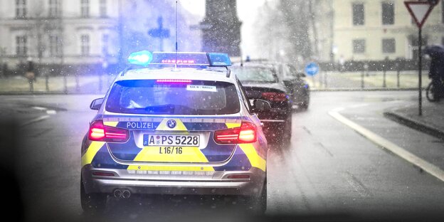 ein Polizeiauto von hinten mit Blaulicht fährt durch ein winterliches München ein Polizeiauto von hinten mit Blaulicht fährt durch ein winterliches München