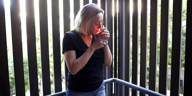 Frau zündet sich eine Zigarette an. Sie steht vor einem hohen Metallgitterzaun Frau zündet sich eine Zigarette an. Sie steht vor einem hohen Metallgitterzaun