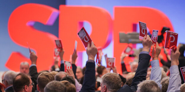 Vor dem Logo der SPD heben Menschen die Stimmkarten in die Höhe Vor dem Logo der SPD heben Menschen die Stimmkarten in die Höhe