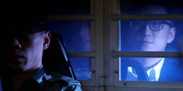 Edward Leung blickt hinter einem Autofenster hervor, vor ihm sitzt ein Polizist am Steuer Edward Leung blickt hinter einem Autofenster hervor, vor ihm sitzt ein Polizist am Steuer