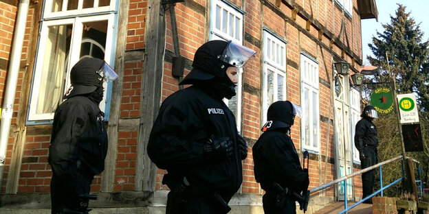 Vier vermummte Polizisten stehen in schwarzer Kampfmontor vor einem alten Backsteinhaus. Vier vermummte Polizisten stehen in schwarzer Kampfmontor vor einem alten Backsteinhaus.