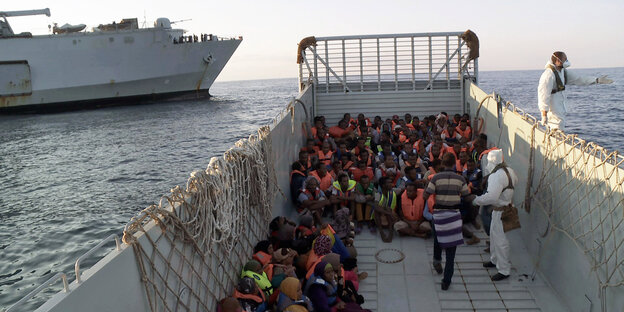 Geflüchtete sitzen in roten Rettungswesten auf einem Boot Geflüchtete sitzen in roten Rettungswesten auf einem Boot