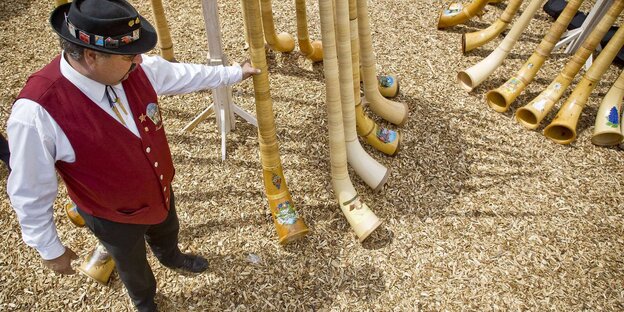 Ein Mann in mit traditionellem Hut und Weste steht neben mehreren Alphörnern Ein Mann in mit traditionellem Hut und Weste steht neben mehreren Alphörnern