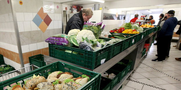 Mehrere Menschen stehen an Kisten voller Essen Mehrere Menschen stehen an Kisten voller Essen