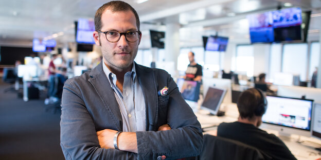 Ein Mann steht mit verschränkten Armen in einem Newsroom