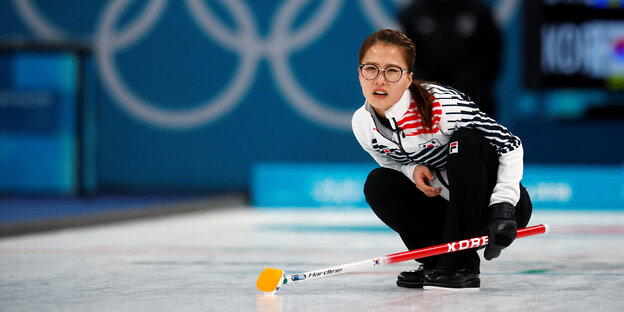 Eine Curling-Spielerin hockt nach ihrem Zug auf dem Eis Eine Curling-Spielerin hockt nach ihrem Zug auf dem Eis