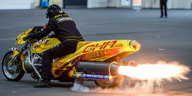 Ein Mann sitzt auf einem gelben Motorrad, aus dessen Auspuff eine Stichflamme kommt Ein Mann sitzt auf einem gelben Motorrad, aus dessen Auspuff eine Stichflamme kommt