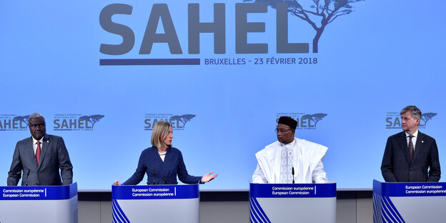 Vor einer Leinwand, auf die in großen Lettern "Sahel" projeziert wird, stehen drei Männer und eine Frau an Podien