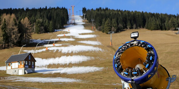eine Skipiste die spärlich mit Kunstschnee bedeckt ist, im Vordergrund eine Schneekanone eine Skipiste die spärlich mit Kunstschnee bedeckt ist, im Vordergrund eine Schneekanone