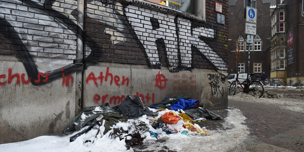 Verschiedene Decken eines Obdachlosen liegen vor einer mit Graffiti besprühten Hauswand. Auf den Decken liegt teilweise Schnee. Verschiedene Decken eines Obdachlosen liegen vor einer mit Graffiti besprühten Hauswand. Auf den Decken liegt teilweise Schnee.