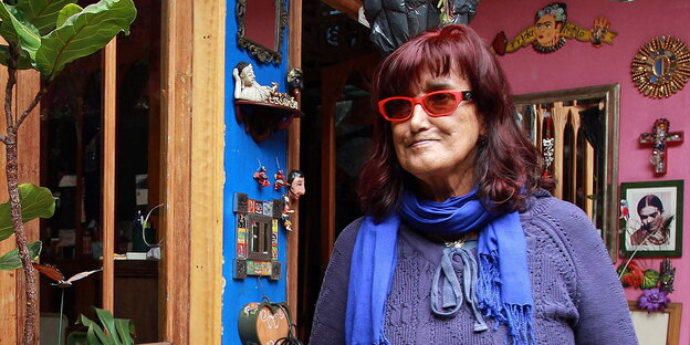 Patricia Ariza steht lächelnd in einem bunten Raum voller Blumen Patricia Ariza steht lächelnd in einem bunten Raum voller Blumen