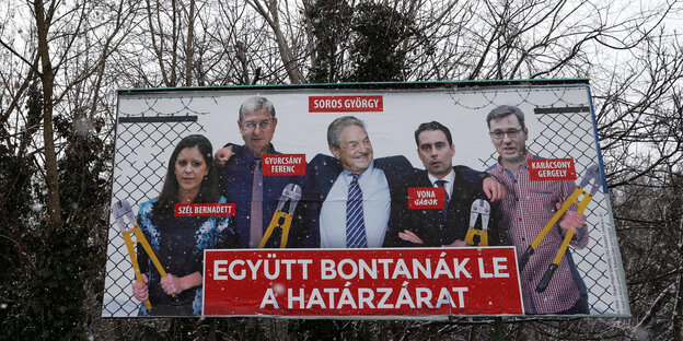 Ein Werbeplakat, auf dem mehrere Menschen zu sehen sind, dahinter kahle Bäume Ein Werbeplakat, auf dem mehrere Menschen zu sehen sind, dahinter kahle Bäume