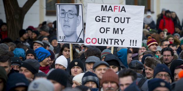 Eine Menschenmenge, aus der Schilder in die Höhe ragen. Auf einem steht „Mafia, get out of my country“ Eine Menschenmenge, aus der Schilder in die Höhe ragen. Auf einem steht „Mafia, get out of my country“