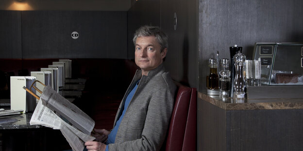 Ein Mann sitzt an einem Tisch und hält eine Zeitung in der Hand Ein Mann sitzt an einem Tisch und hält eine Zeitung in der Hand