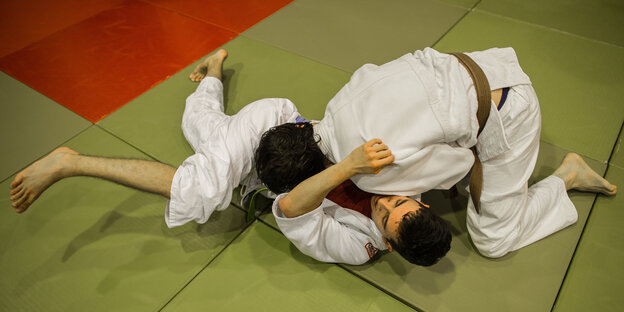 Zwei junge Männer kämpfen in Judo-Anzügen auf dem Boden einer Turnhalle. Zwei junge Männer kämpfen in Judo-Anzügen auf dem Boden einer Turnhalle.
