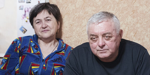 Eine Frau und ein Mann sitzen vor einer beigen Wand Eine Frau und ein Mann sitzen vor einer beigen Wand