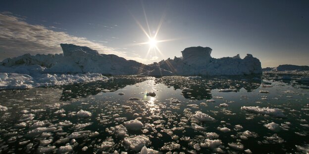 Eisberge und Eisschollen im Meer, die Sonne strahlt vom Himmel Eisberge und Eisschollen im Meer, die Sonne strahlt vom Himmel